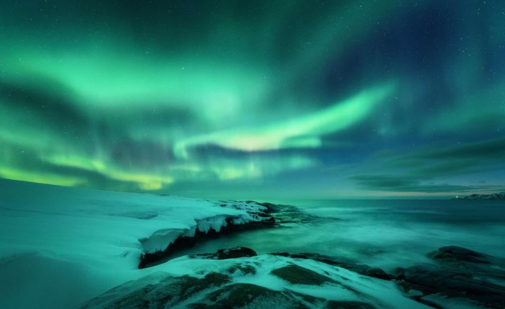 Green northern lights above snowy rocks