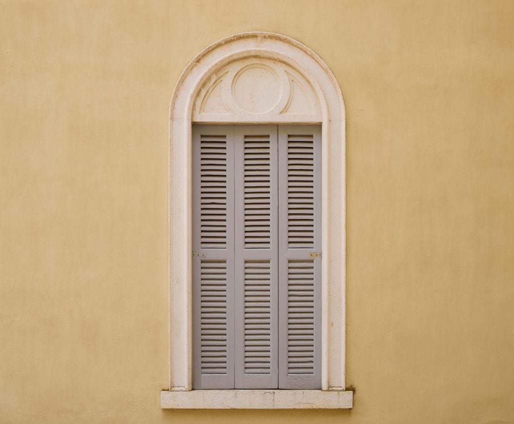Window with wooden shutters on yellow wall