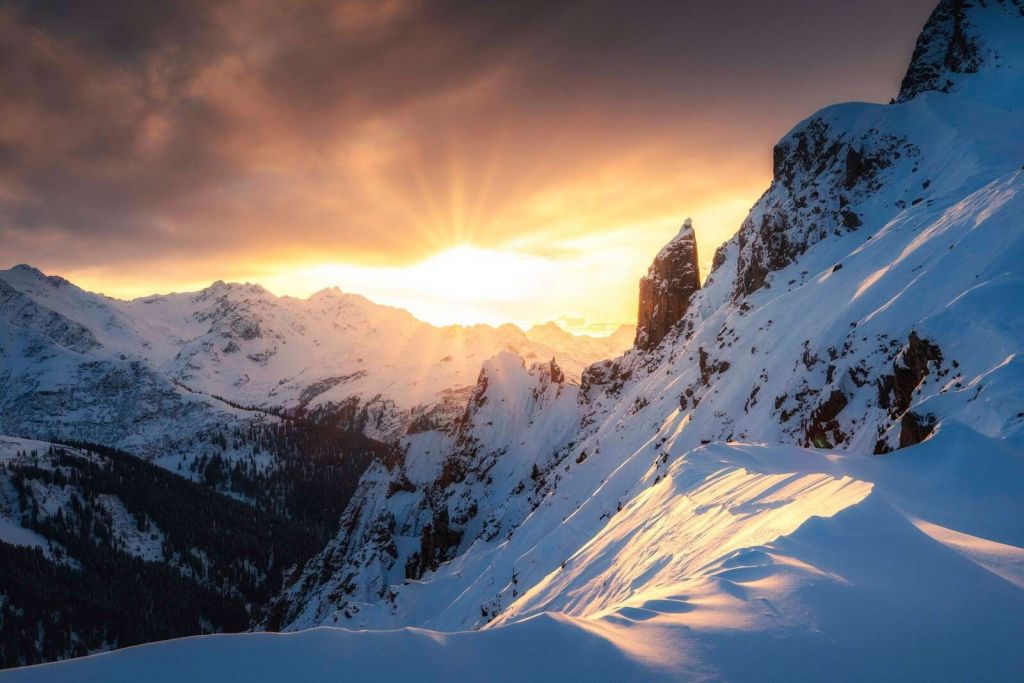 Evening sun behind snow-capped mountain peaks