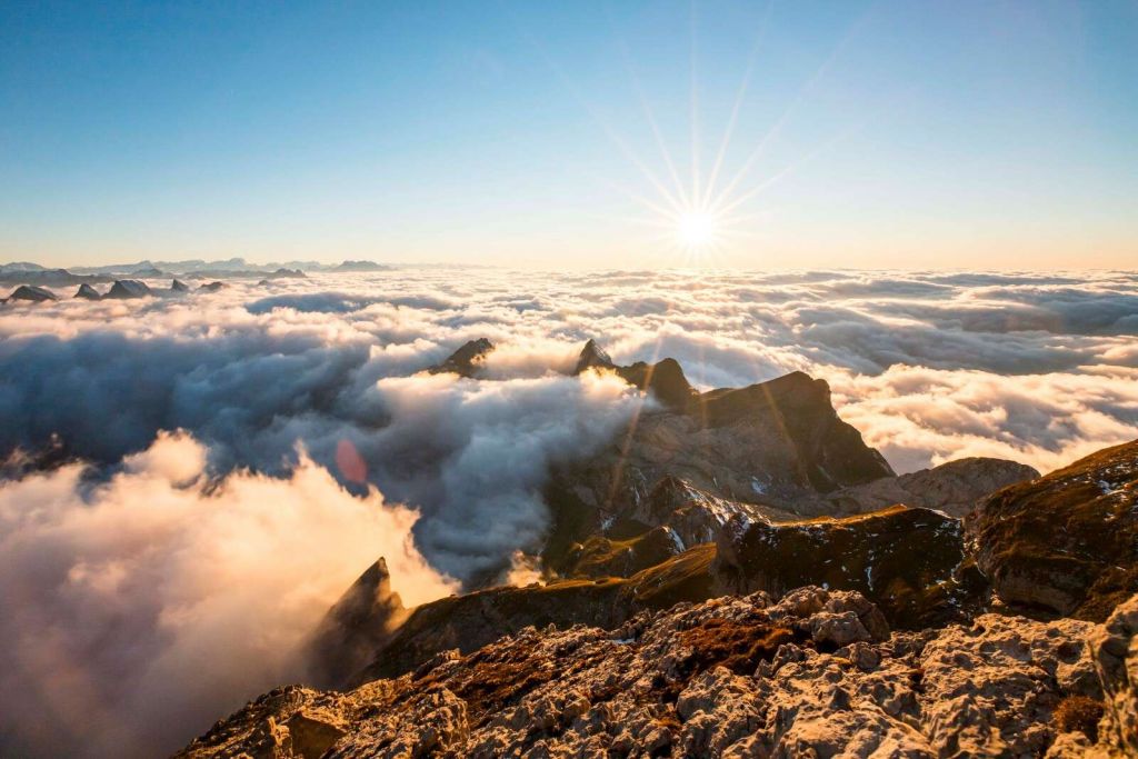 Sun above cloud cover and mountain peaks
