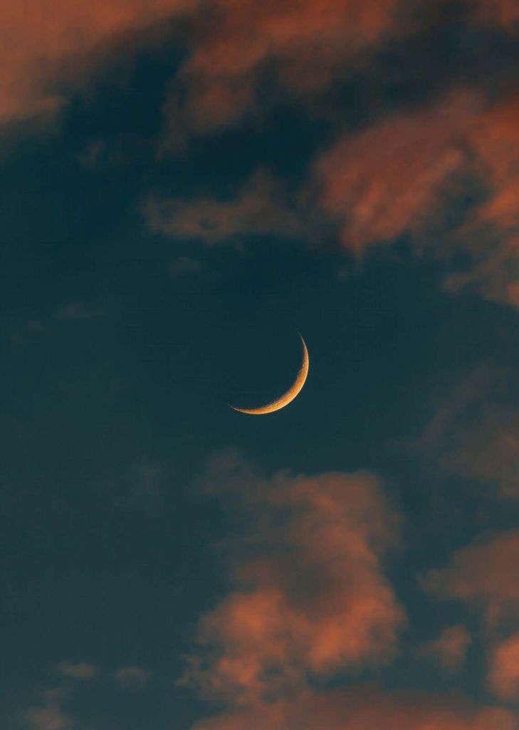 Slim crescent moon among fiery clouds