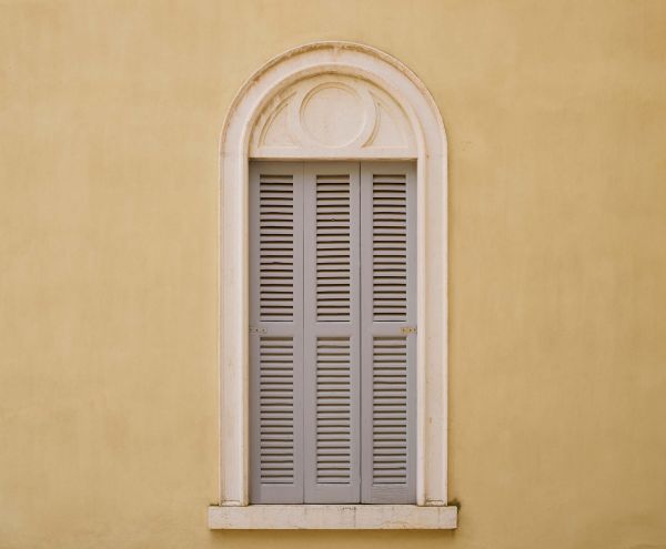 Window with wooden shutters on yellow wall