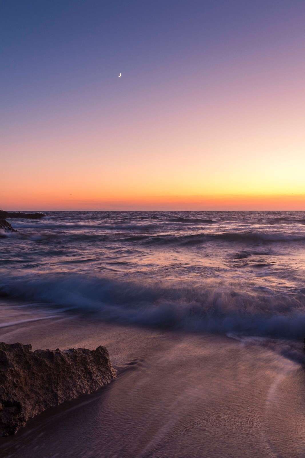 Moonlight above purple waves at sunset